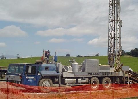 WellDrillers truck-mounted rotary drilling rig with its mast raised on a farm site