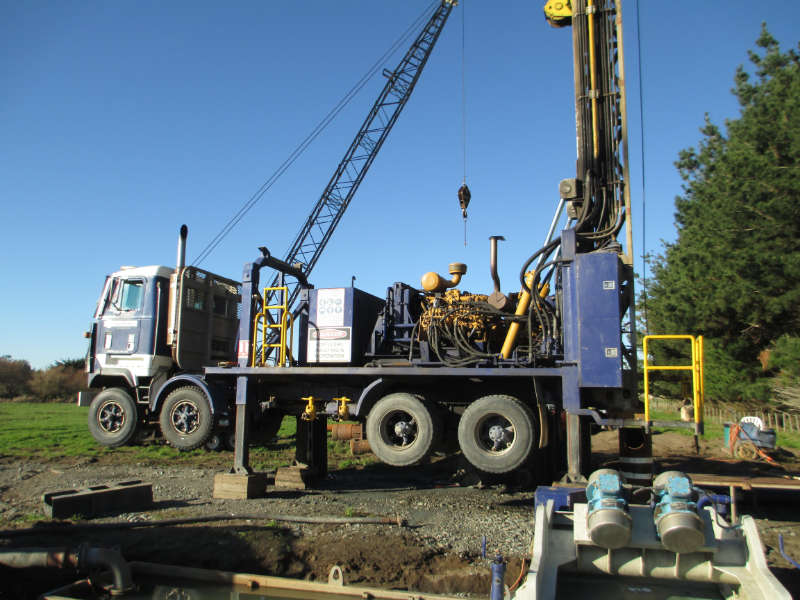 truck 1 WellDrillers truck-mounted drilling rig with crane and mast raised over a farm bore